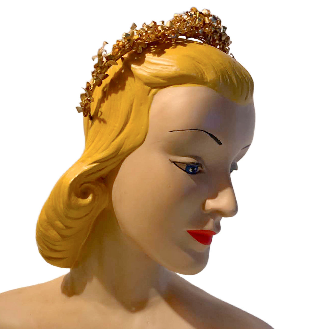A vintage-style gold tiara with leaf-like detailing, shown on a blonde mannequin head against a plain white background.